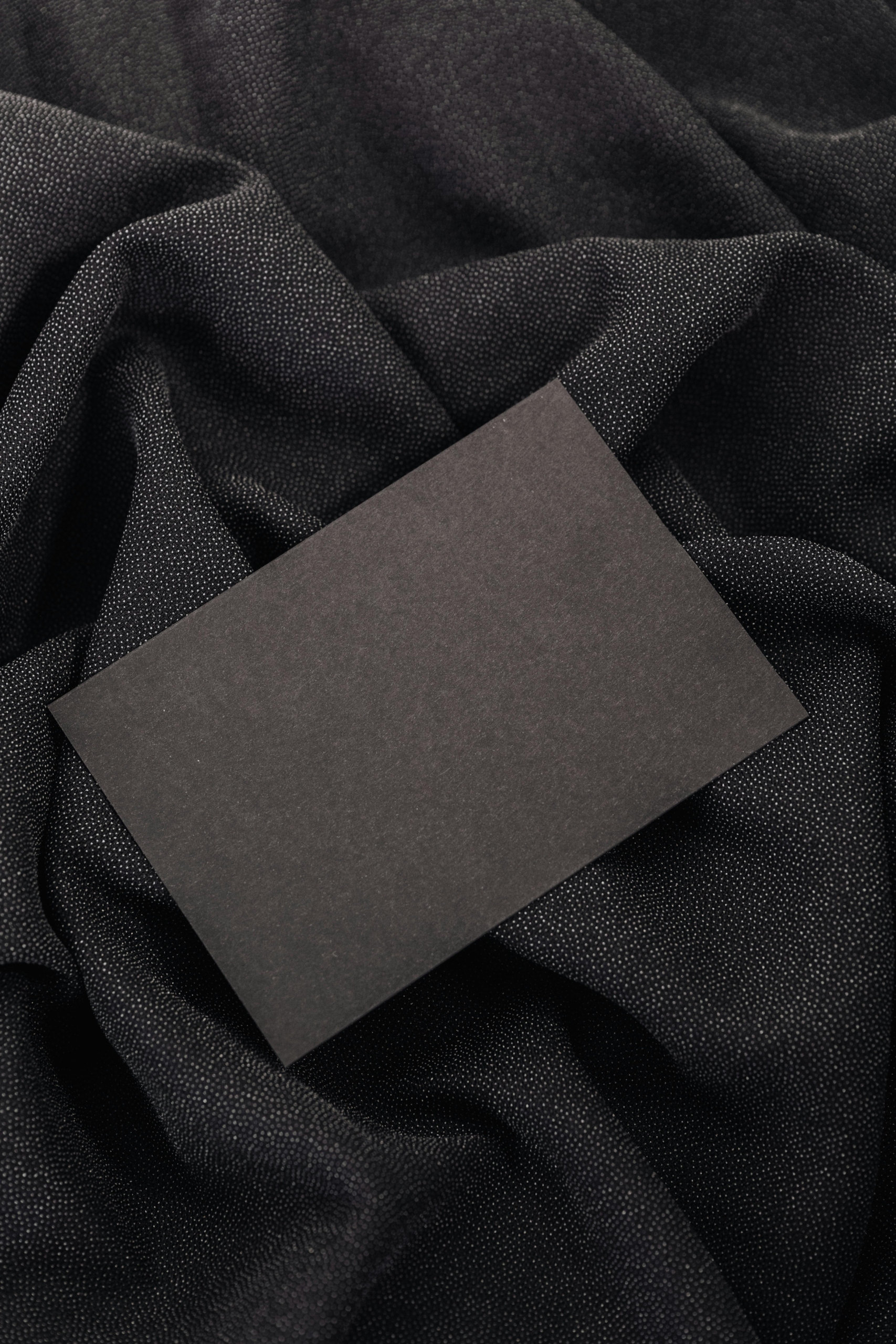 Black card on textured black fabric background, ideal for mockups and design presentations.